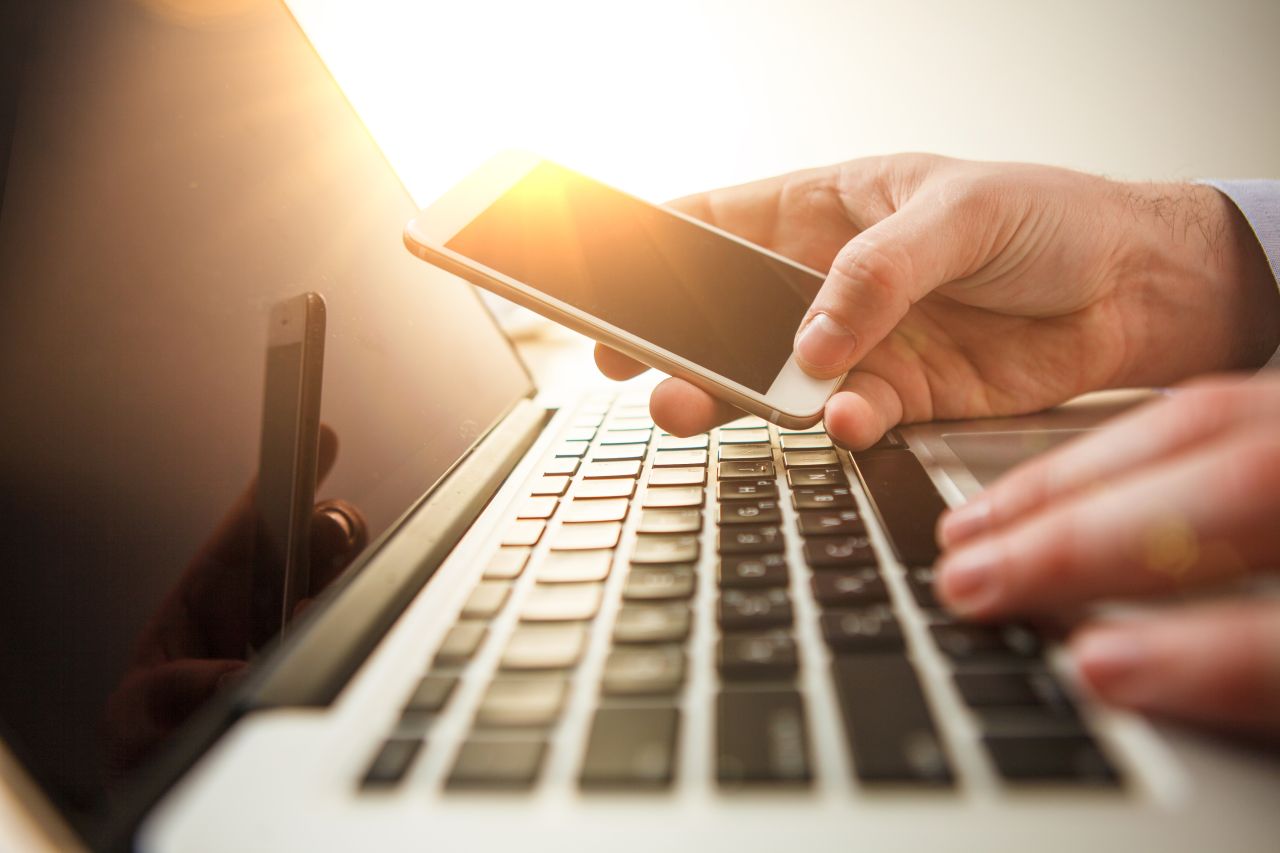 The male hand holding a phone against the background of the office and laptop